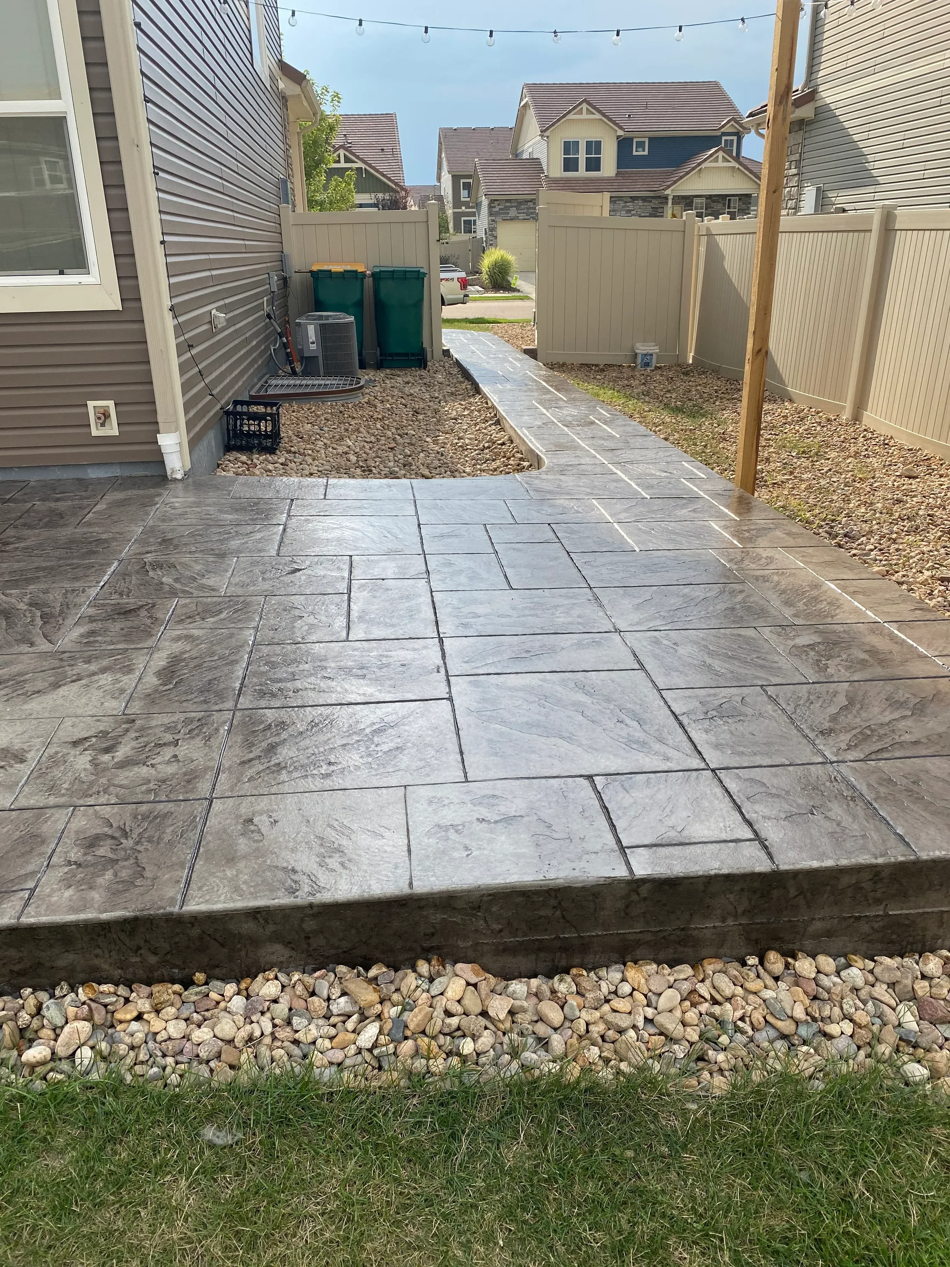 Gray stamped concrete patio with ashlar slate pattern, gravel borders, and metal pergola overhead